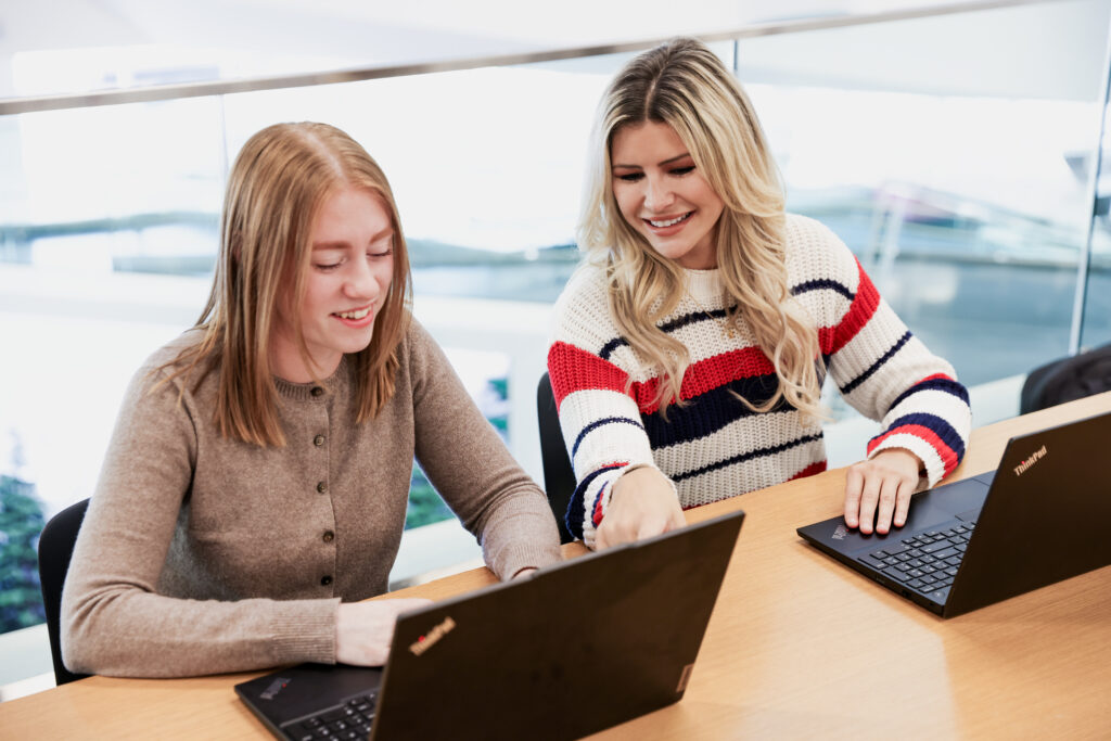 Two women collaborating on laptops at office table