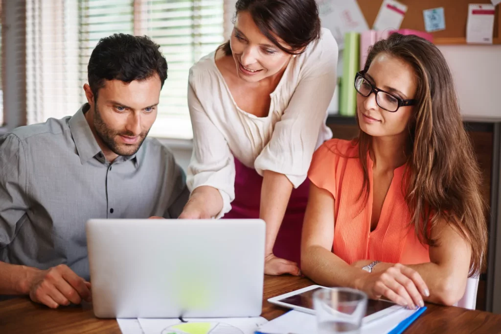 Three coworkers collaborating around laptop in office