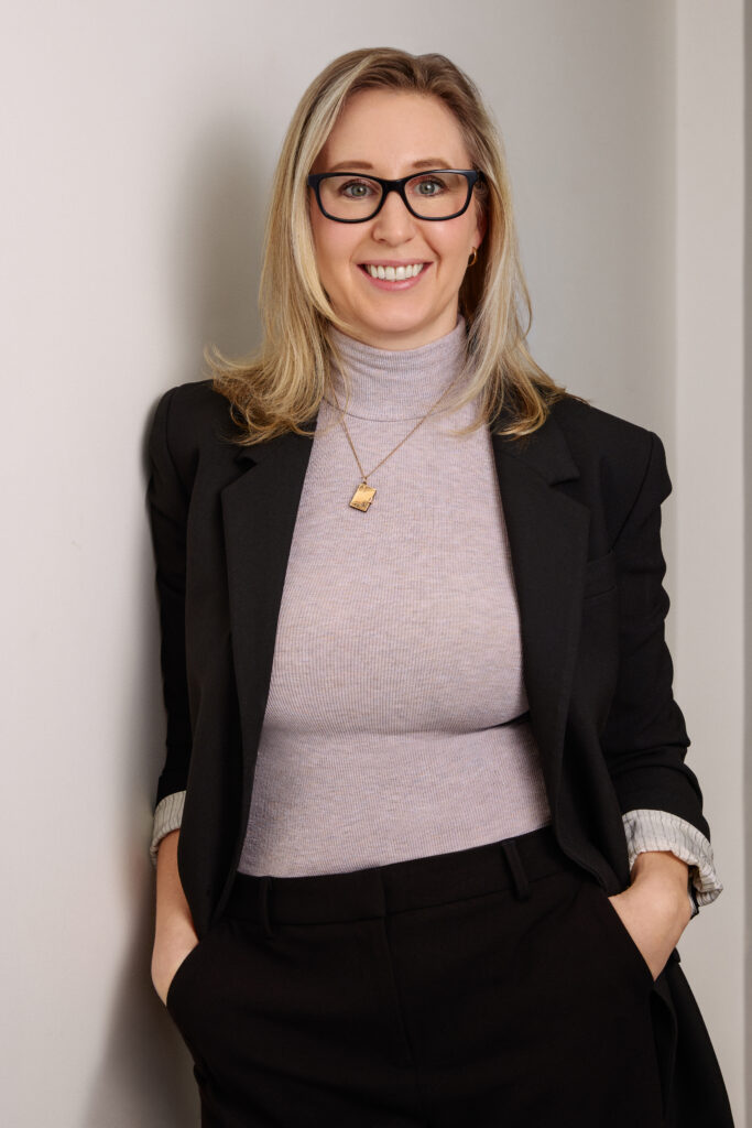 Professional woman in glasses smiling against wall