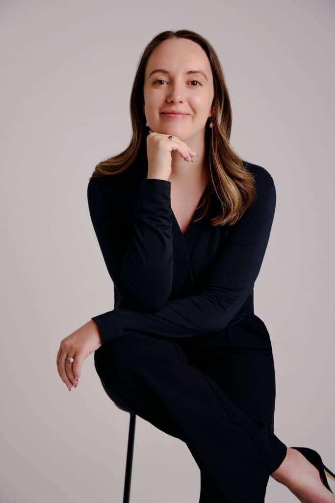 Woman in black outfit seated against a light background